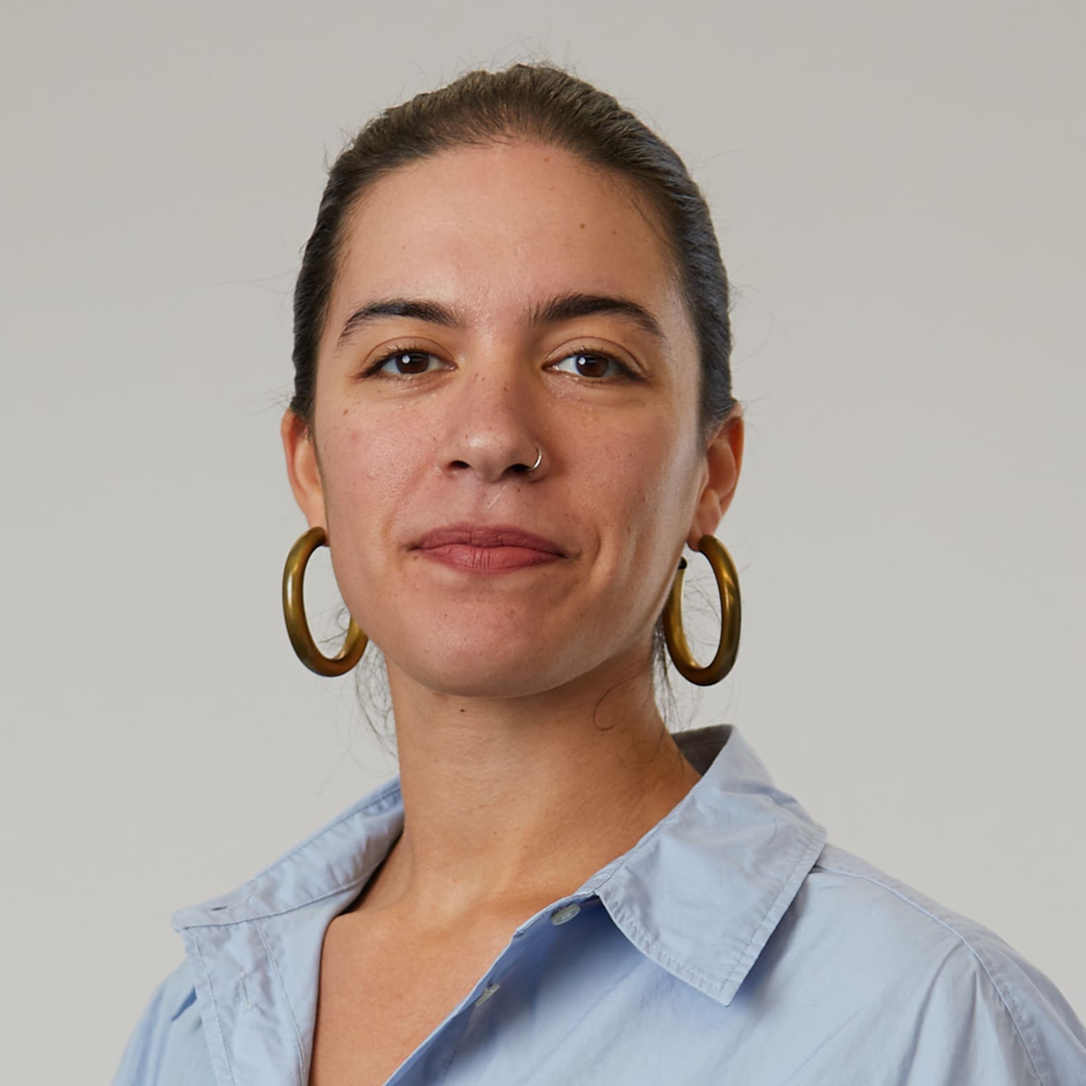 Woman with dark hair pulled back wearing gold hoop earrings and light blue collared shirt