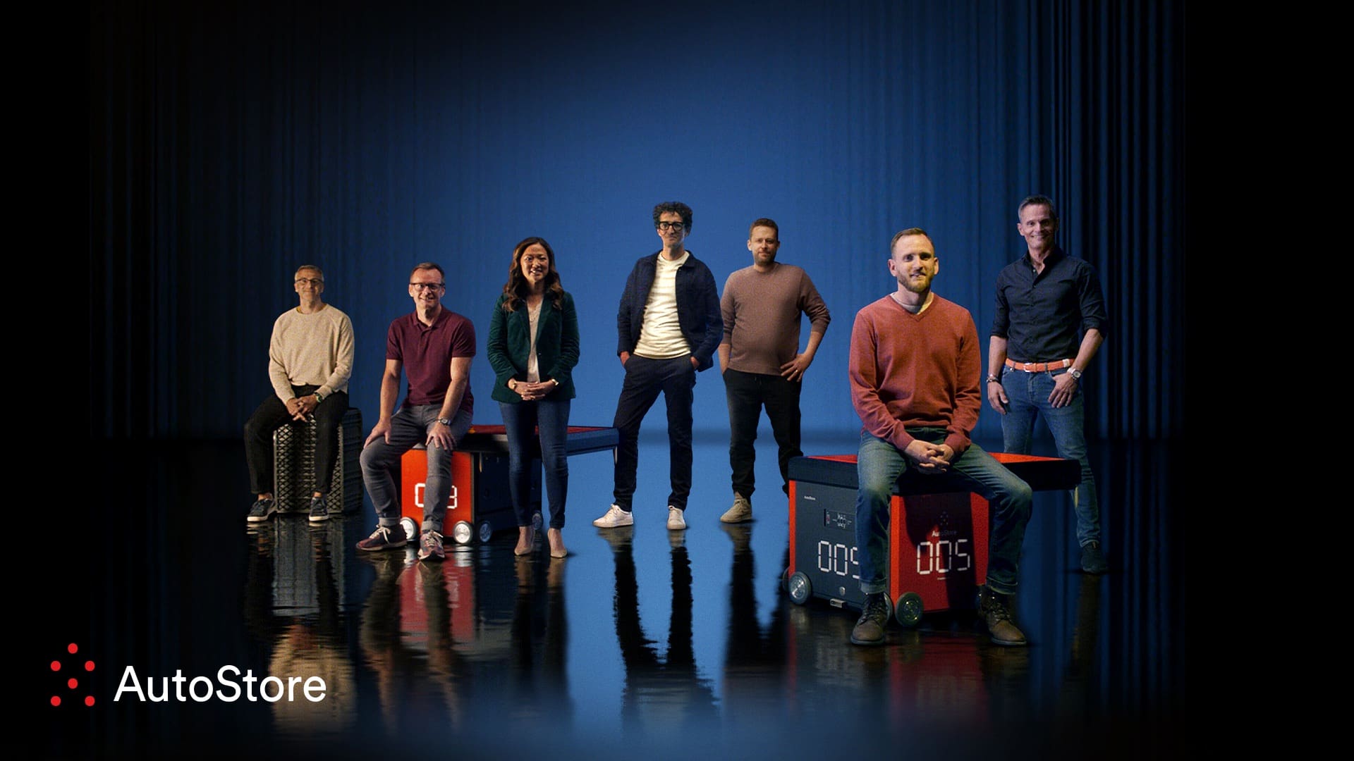 Eight people pose on boxes with "AutoStore" logo and numbers displayed, against a blue backdrop.