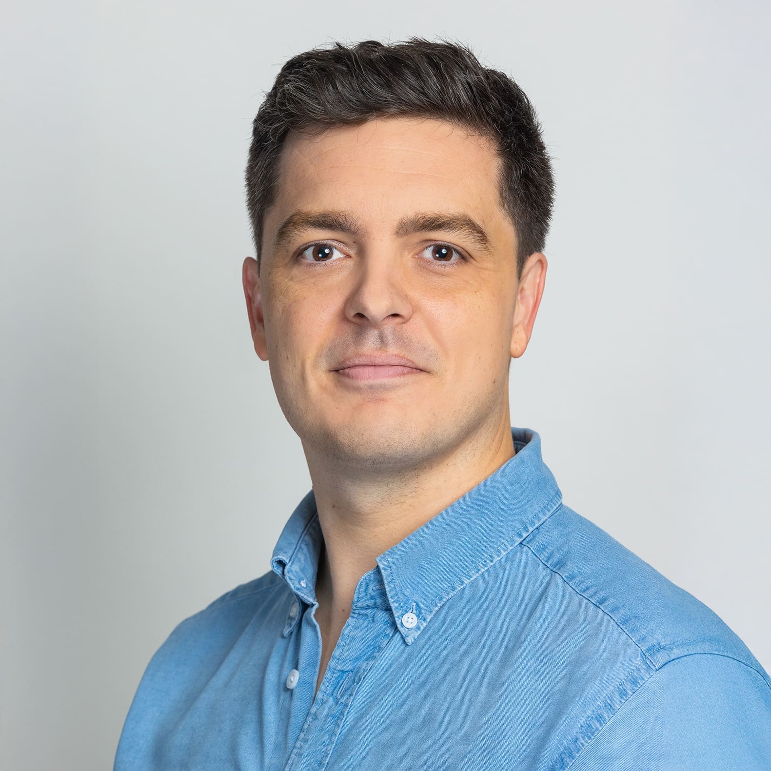 Man with short dark hair in a light blue shirt against a light gray background.
