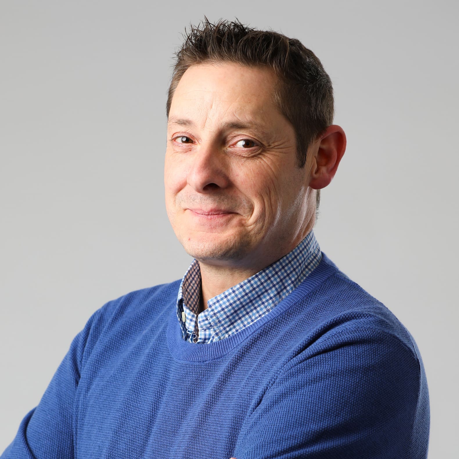 Smiling man in a blue sweater, with arms crossed, against a gray background.