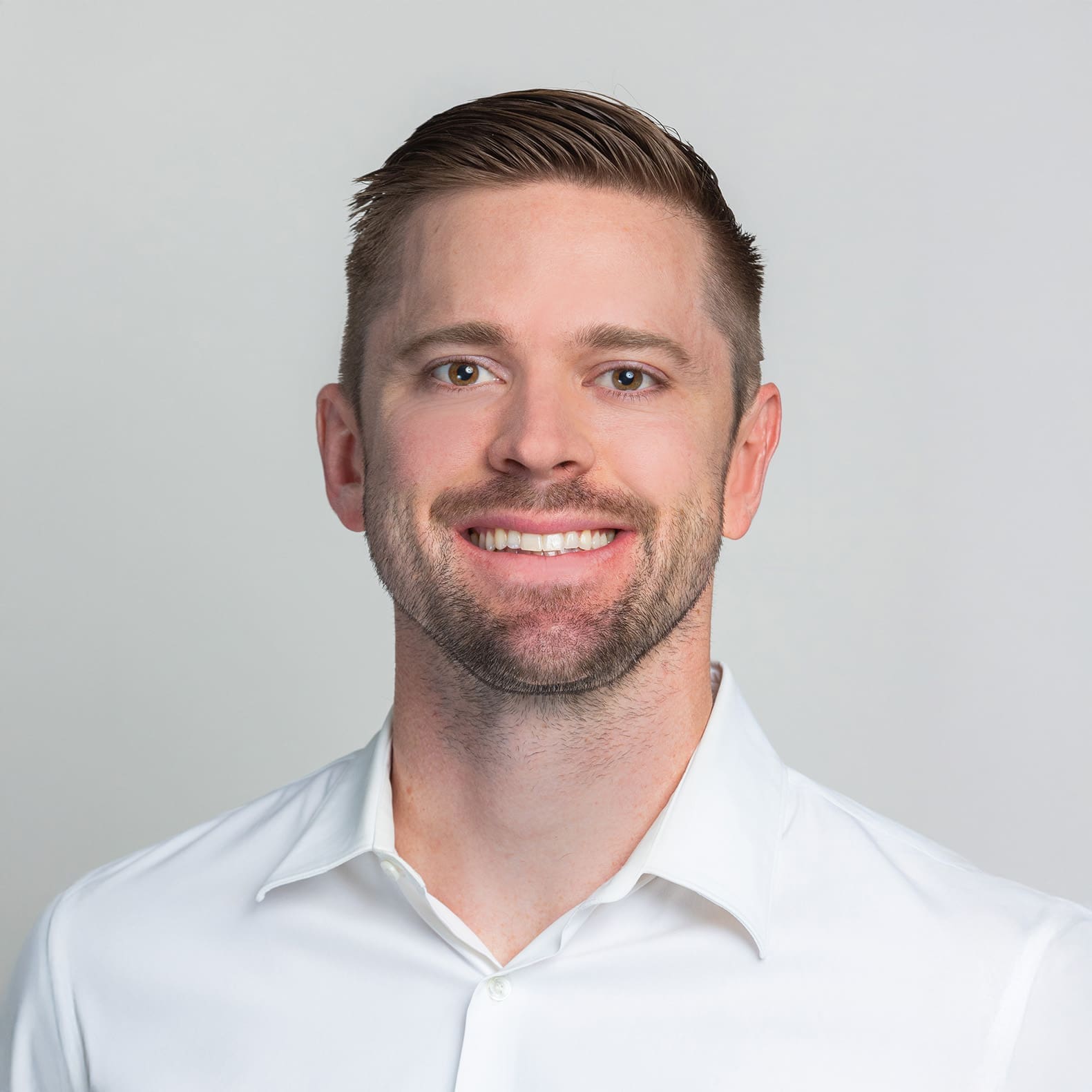 Professional headshot of a smiling man with brown hair and beard wearing a white collared shirt