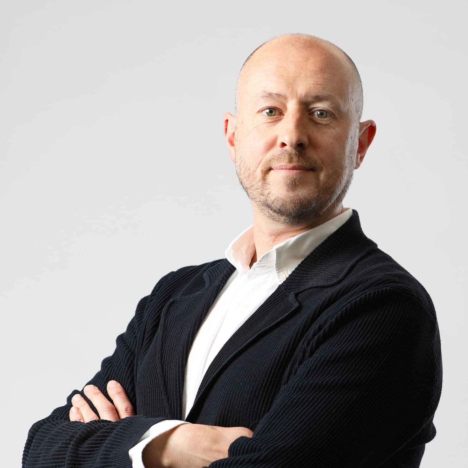Professional headshot of bald man in dark blazer and white shirt with arms crossed