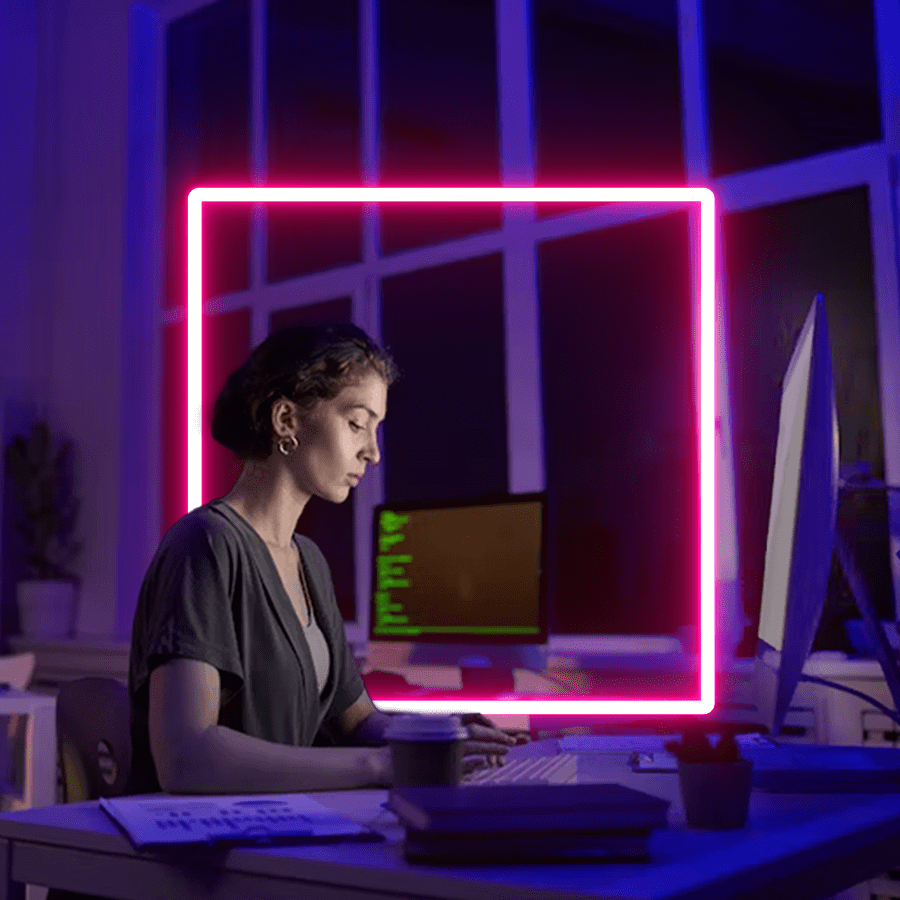 A lady sat working in a dark office between two screens. She is framed by the Transmission pink 'portal' device.