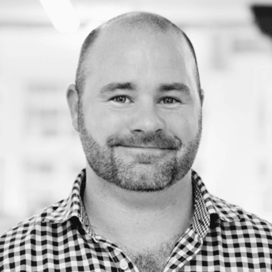 Smiling man with a beard, wearing a checkered shirt, against a blurred background.